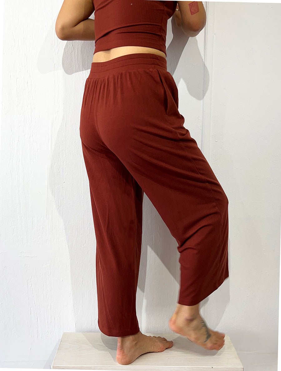 Back view of model wearing simulacra's rib flow pant in the color brick