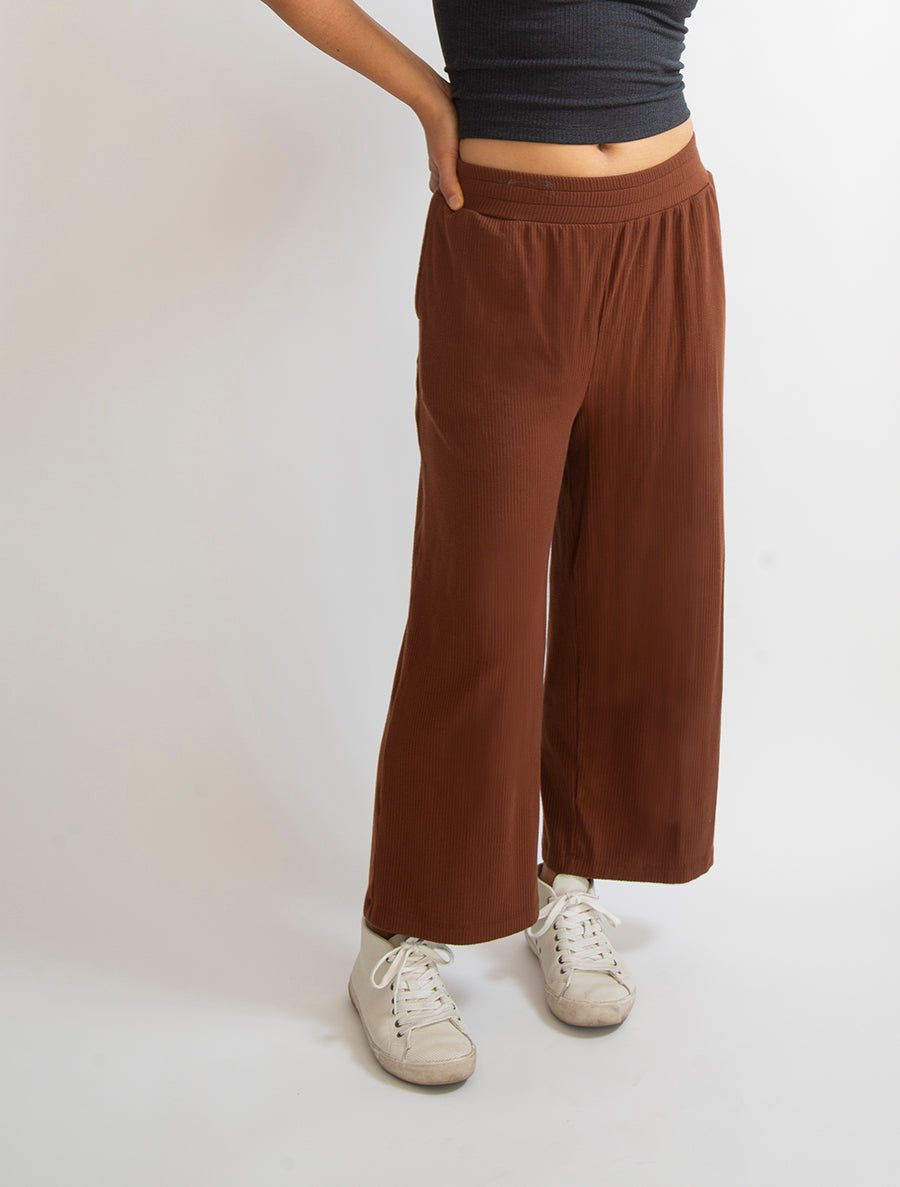 Left quarter view of model wearing simulacra's rib flow pant in the color caramel