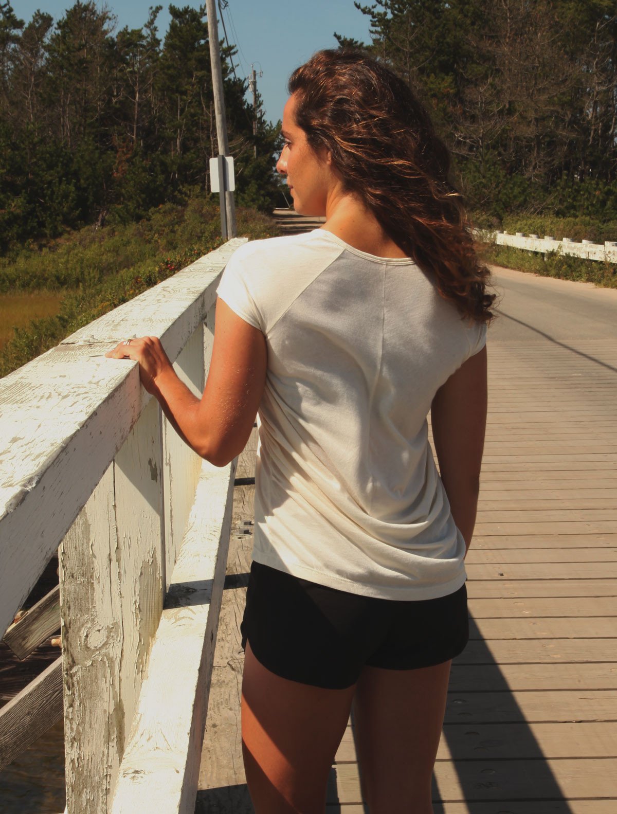 Back view of model wearing simulacra's Draped back T-shirt in natural paired with shorts on bridge.