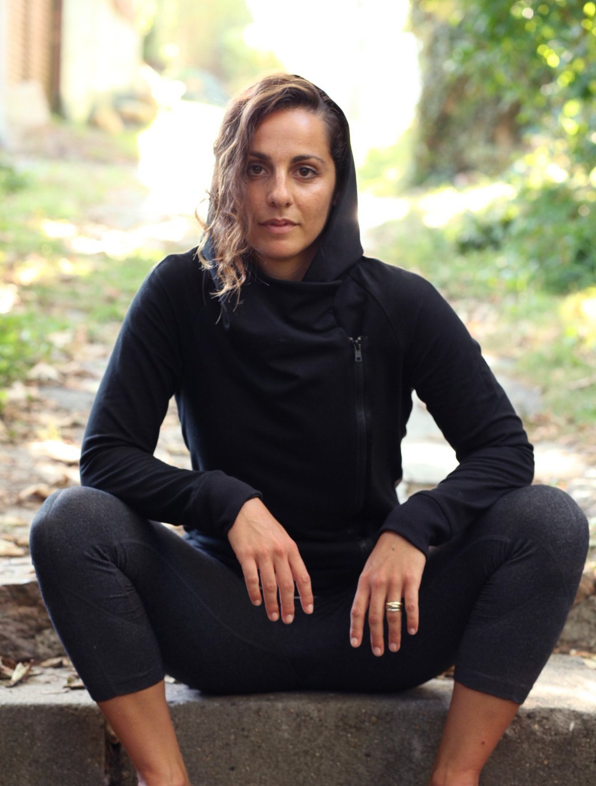 Model relaxing in a wooded field on a stone with front view,  wearing simulacra's Women's Black Cowl Neck Hoodie Sweater