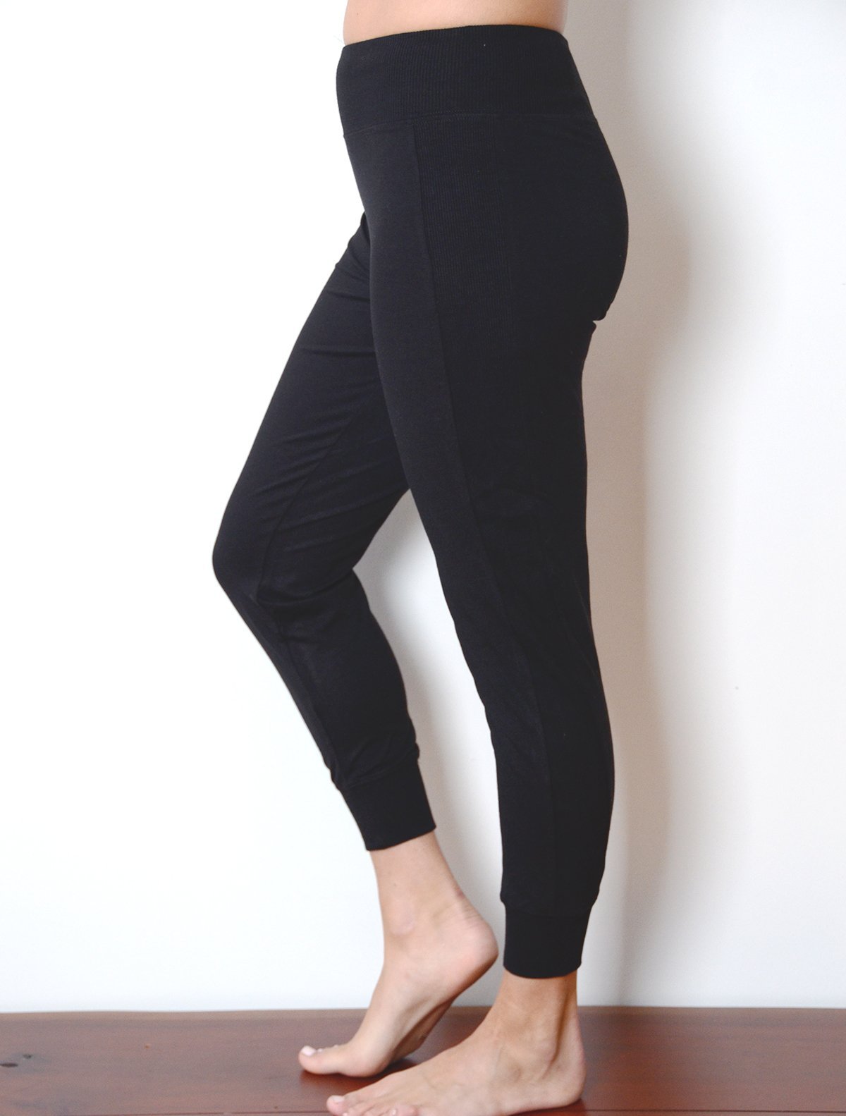 Left side view of model wearing simulacra's women's black cropped joggers with bare stomach to show high rise shape 