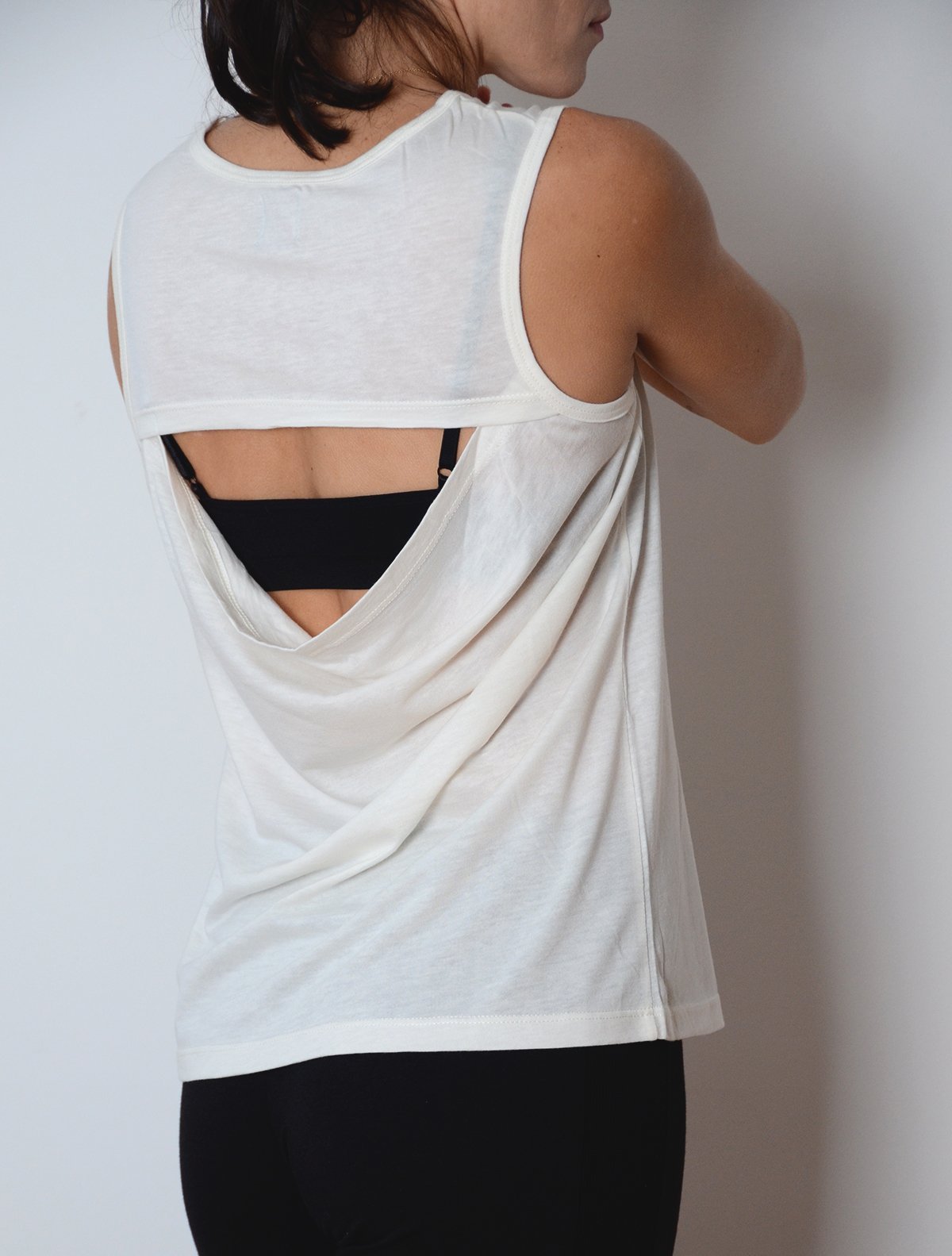 Slightly turned side view of model wearing simulacra's womens organic cotton muscle tank in white