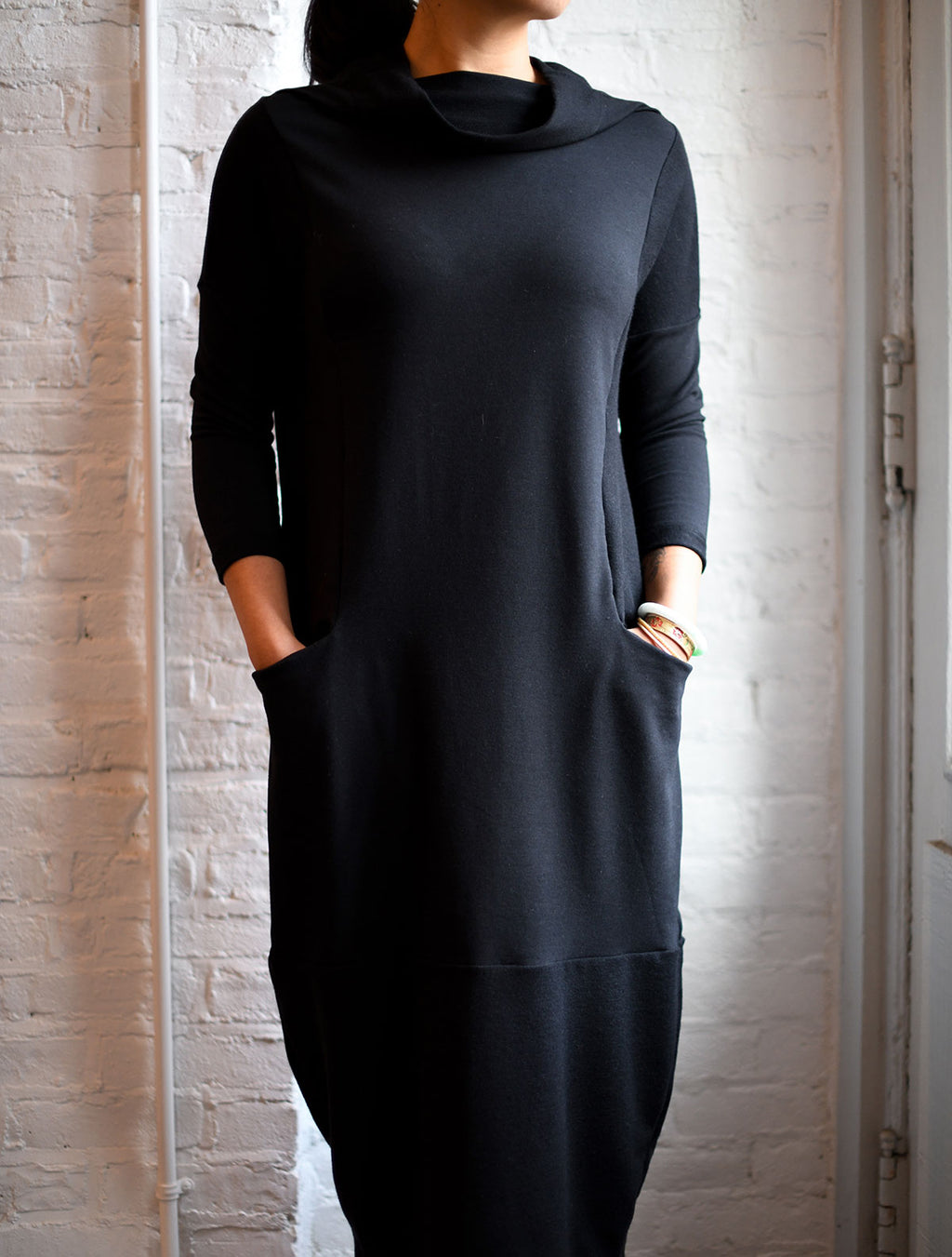 Front view of woman modeling the black funnel neckline cocoon dress with pockets